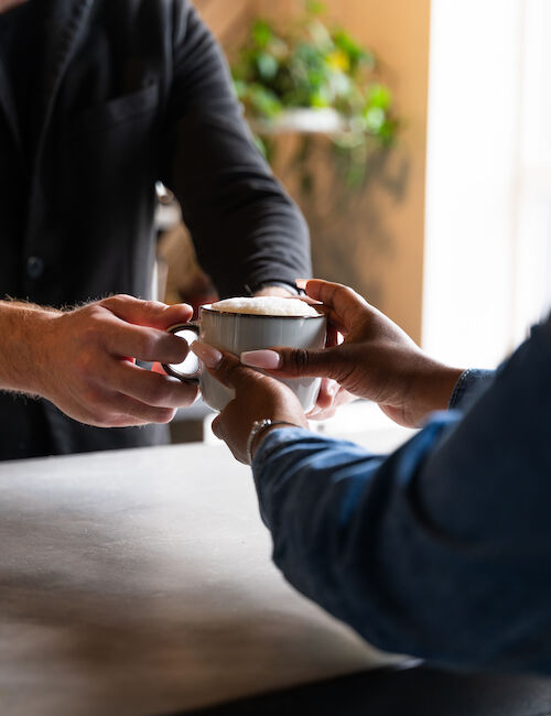 A person is handing a cup of coffee to another person across a counter in what appears to be a café or coffee shop.