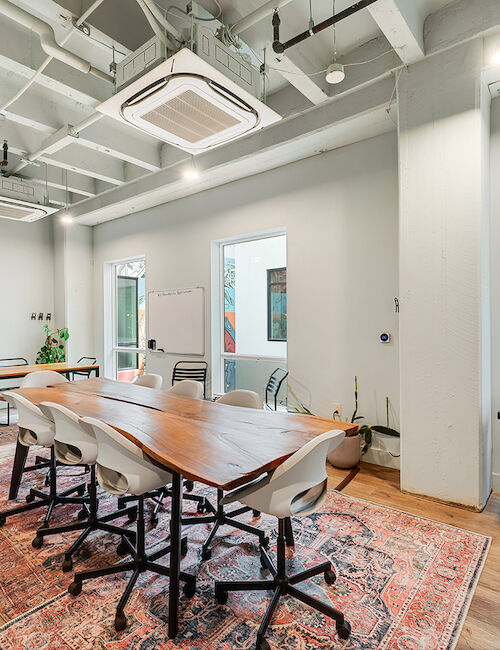 The image showcases a modern conference room with a long wooden table, chairs, and bright lighting, featuring a cozy seating area.