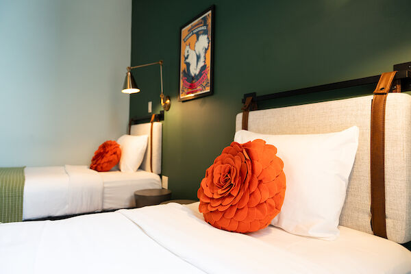 A cozy bedroom with two single beds, each adorned with an orange flower-shaped pillow. There's wall art and a stylish lamp beside the far bed.