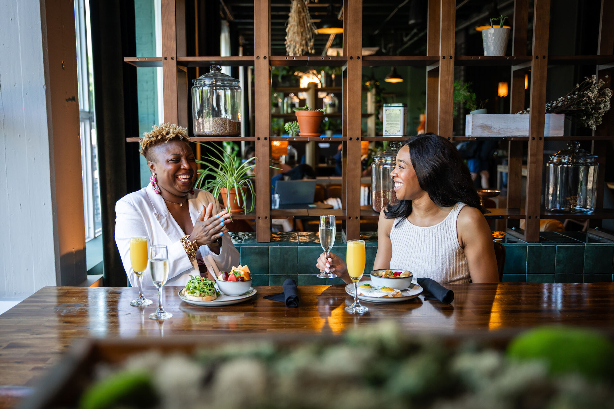 Two women are sitting at a restaurant table, enjoying food and drinks while engaged in conversation.