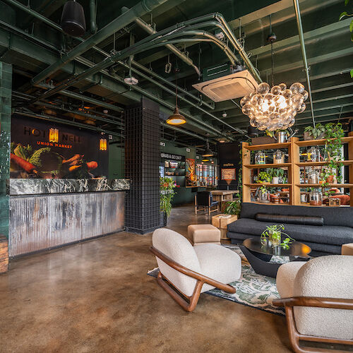 A stylish indoor space with modern furniture, green tiles, a chandelier, plants, a bar area, and a cozy seating arrangement.