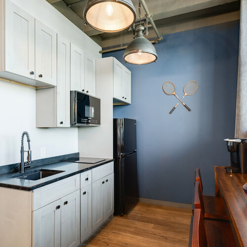 A modern kitchen with white cabinets, black appliances, and two rackets on a blue wall. A bowl with oranges is on the wooden counter, ending the sentence.