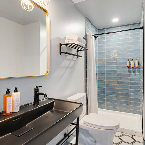 A modern bathroom with a black countertop, a large mirror, a toilet, and a shower with blue tiles and toiletries on the wall.