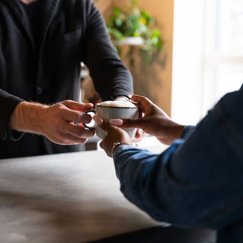 A person is handing a cup of coffee across a counter to another person in what appears to be a café.