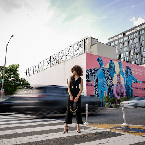 A person stands in front of Union Market, with a colorful mural and blurred cars in the background.