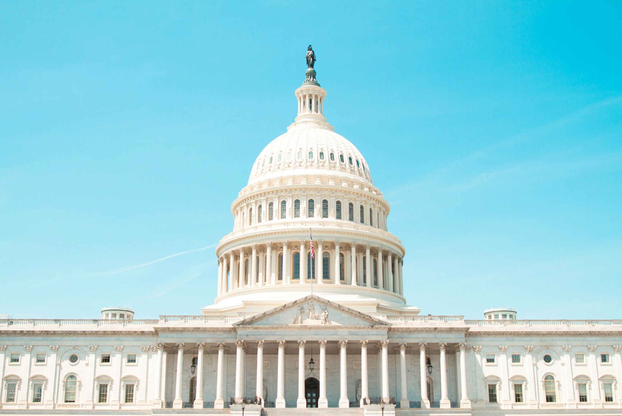 The image shows the United States Capitol building with its iconic dome under a clear blue sky.